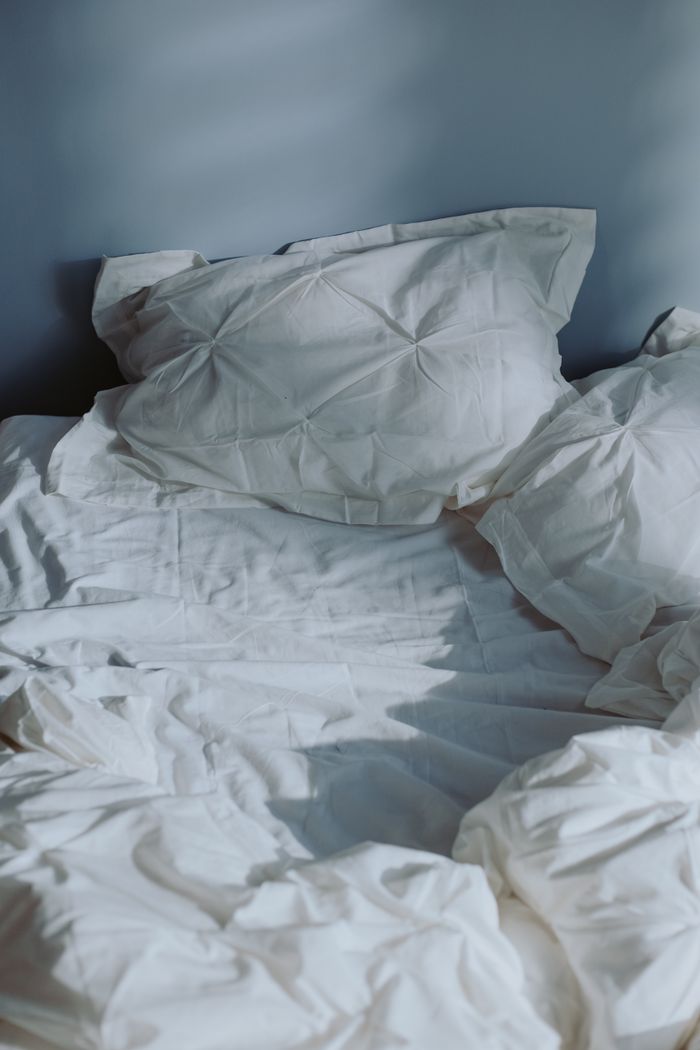 A tranquil scene of an unmade bed with textured white linens capturing morning light.