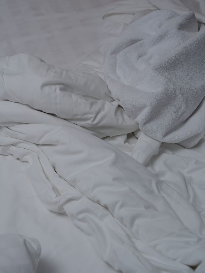 Soft, white bedding in an unmade style, showcasing comfort and relaxation in a subtle, cozy setting.