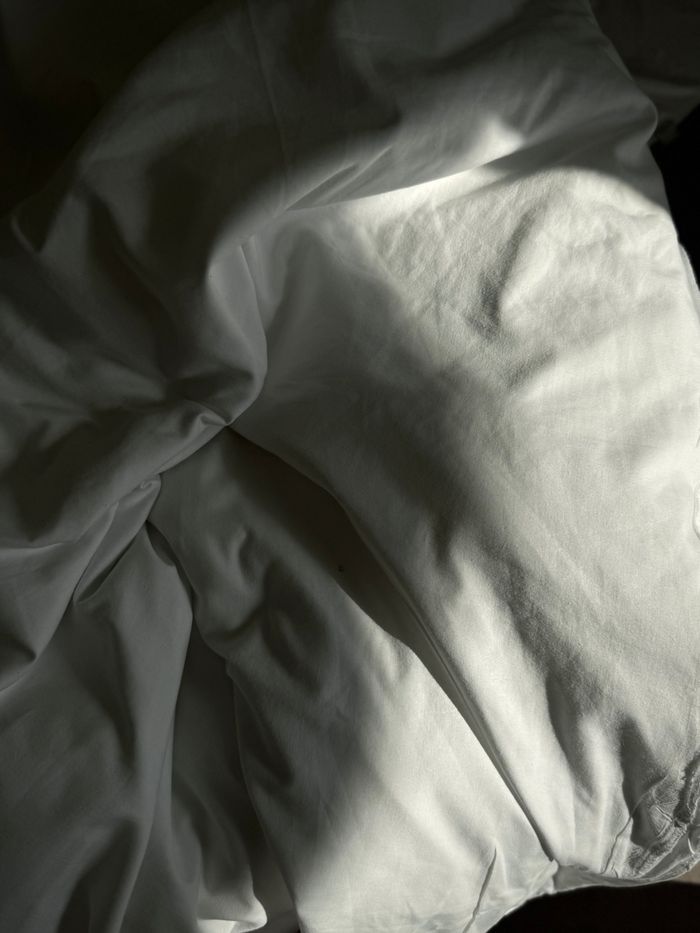 Crumbled white bedding illuminated by morning sun rays, creating a serene and elegant atmosphere.
