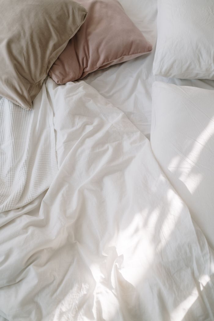 Soft white bedding with sunlight and pillows creating a cozy bedroom atmosphere.