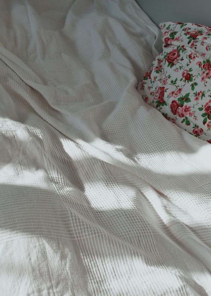 A warm and inviting bed setup with a floral pillow and soft sunlight creating shadows.