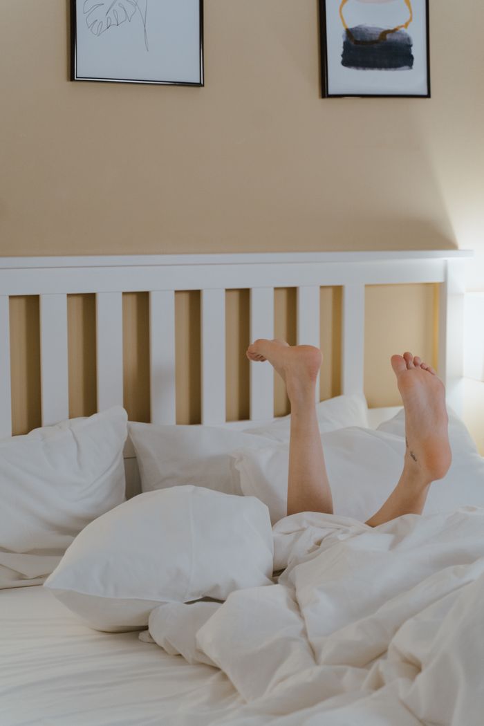 Bare feet peeking from under white sheets in a cozy bedroom, perfect for relaxation themes.