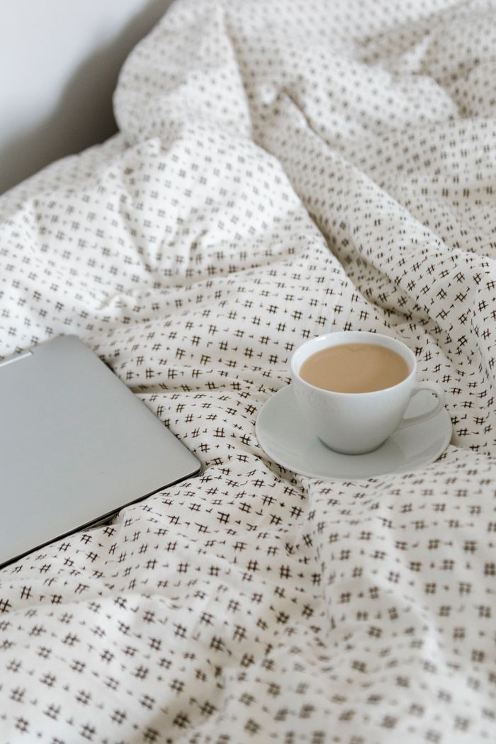 Warm cup of coffee on a bed with a stylish patterned cover. Perfect cozy morning scene.